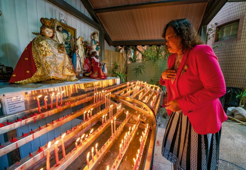 St. Christopher Church secretary Gemma P. Huang lights a candle and silently prays at the shrine outside the church.