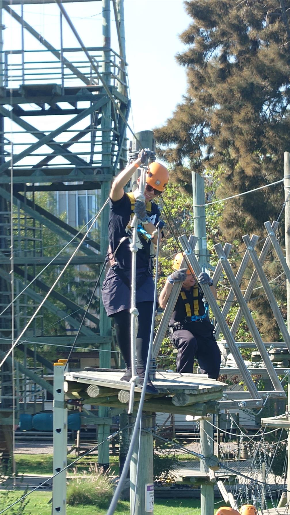 A participant crossing a single-rope bridge over a pond.